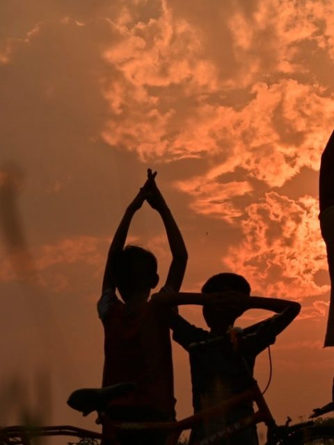 silhouette of 3 person standing beside bicycle during sunset
