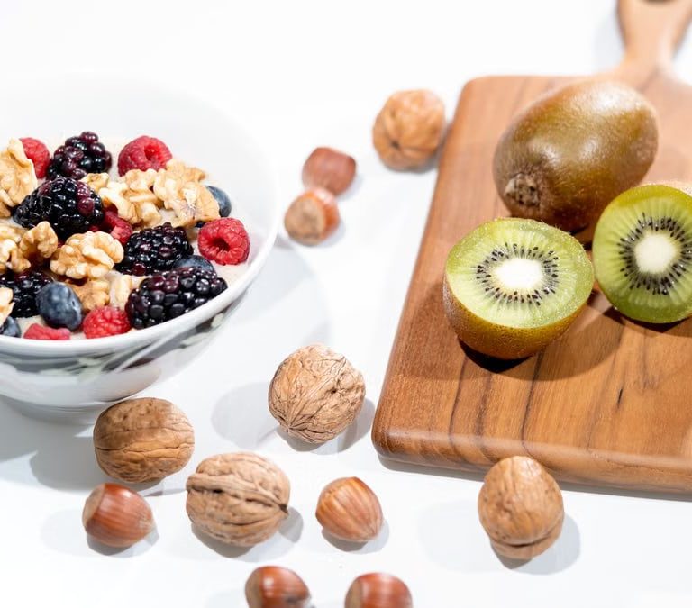 A vibrant bowl of mixed berries, walnuts, and kiwi on a cutting board. Perfect for a healthy breakfast.